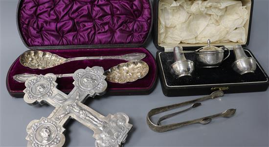 A white metal crucifix (a.f.), a cased silver three piece cruet and two pairs of silver sugar tongs and pair of plated serving spoons